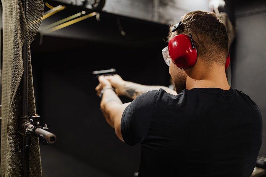 A shooter wearing earmuffs aims a handgun at an indoor shooting range