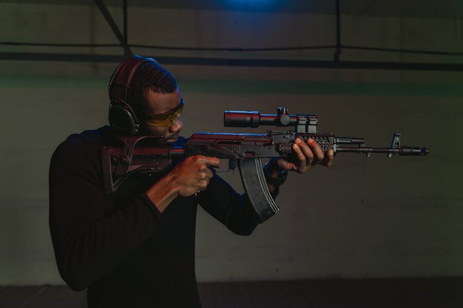 A shooter aiming a rifle at an indoor shooting range, wearing protective ear and eye gear