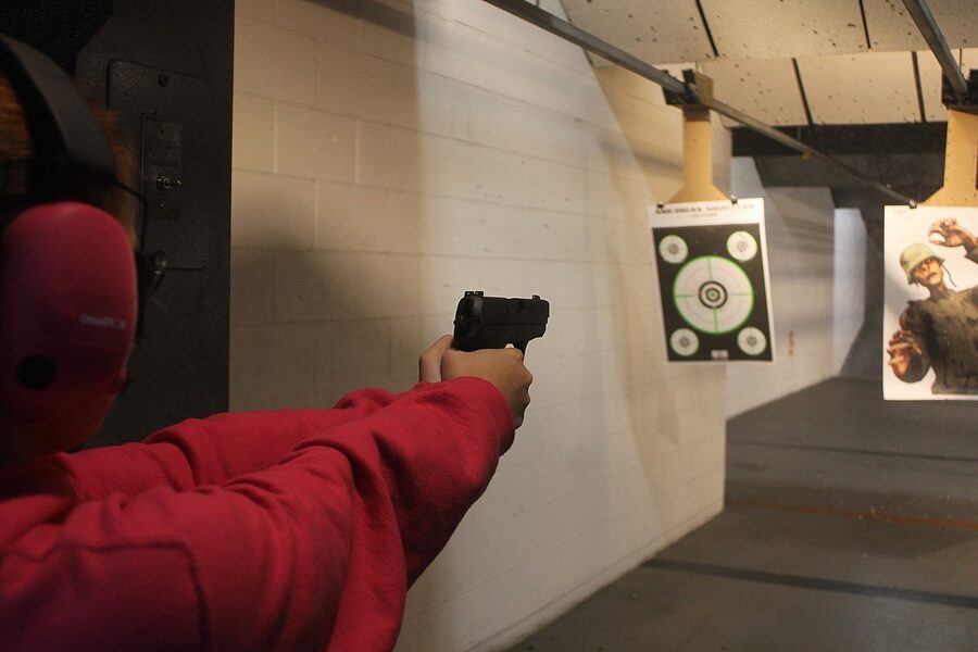 A SIG Sauer P239 pistol being fired by a shooter at an indoor shooting range with full safety gear