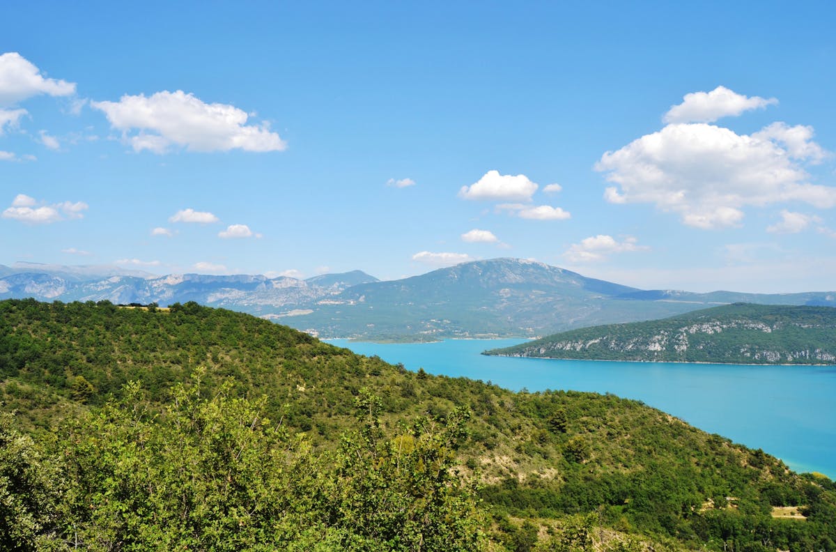 Lake Sainte-Croix surrounded by lush green hills and mountains under a blue sky in Provence