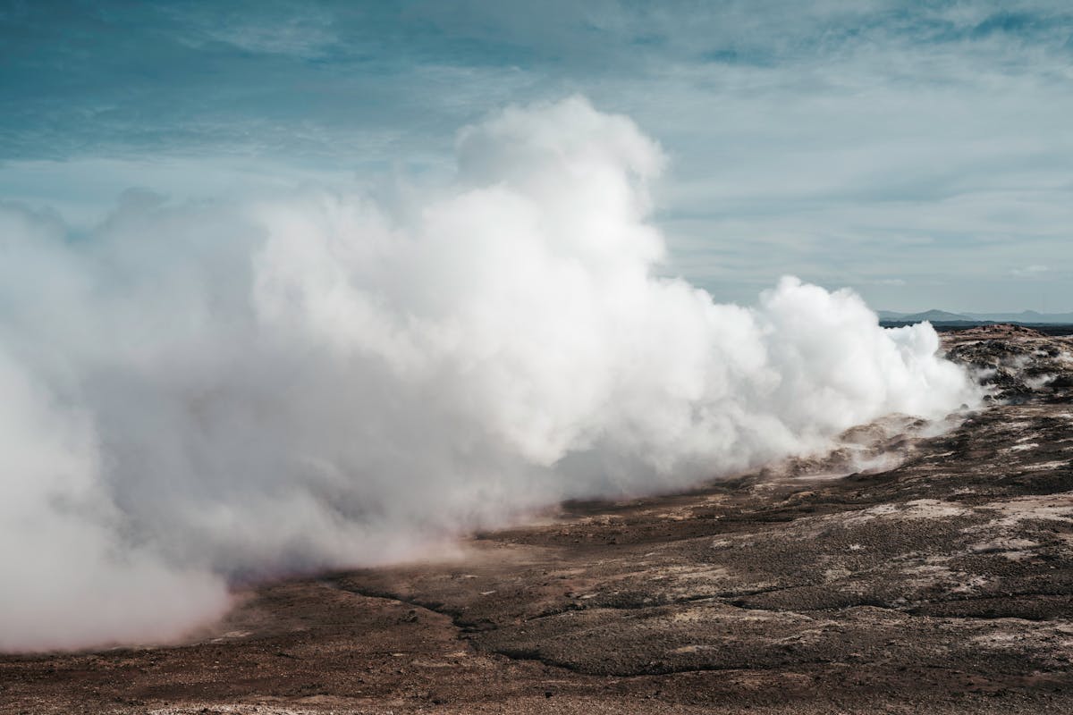 Geothermal steam rising from volcanic terrain in Iceland under clear sky