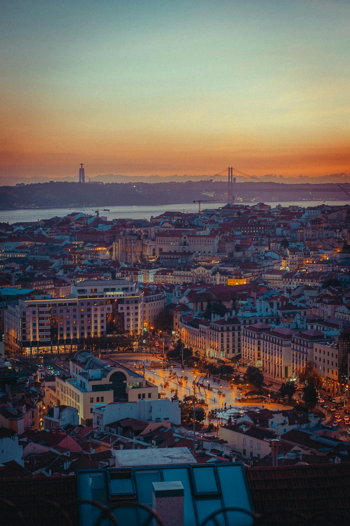 Aerial view of Lisbon at sunset featuring the 25 de Abril Bridge spanning the Tagus River