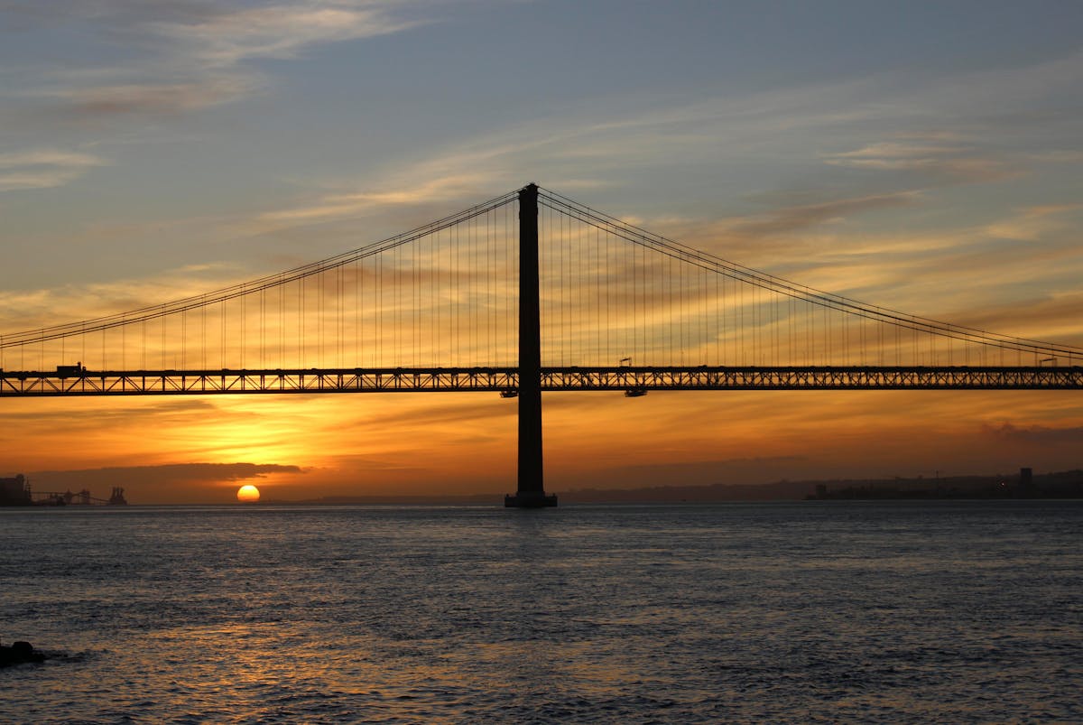 Dark silhouette of the 25 de Abril Bridge against a golden sunset over the Tagus River