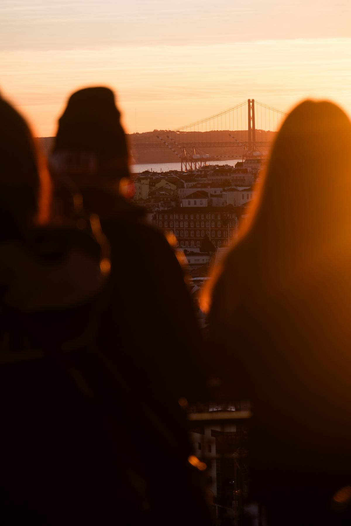 Silhouetted figures watching a golden sunset with a view of a bridge in Lisbon