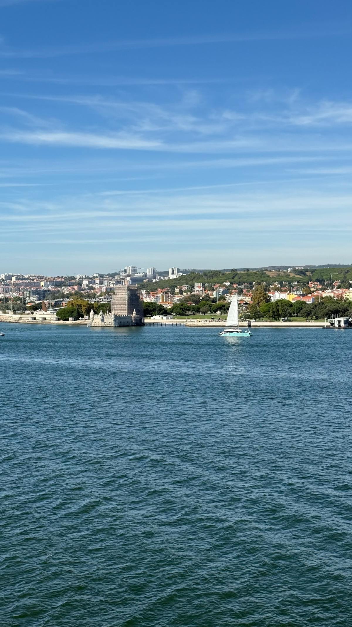 A sailboat gliding past the Belem Tower on a sunny day in Lisbon