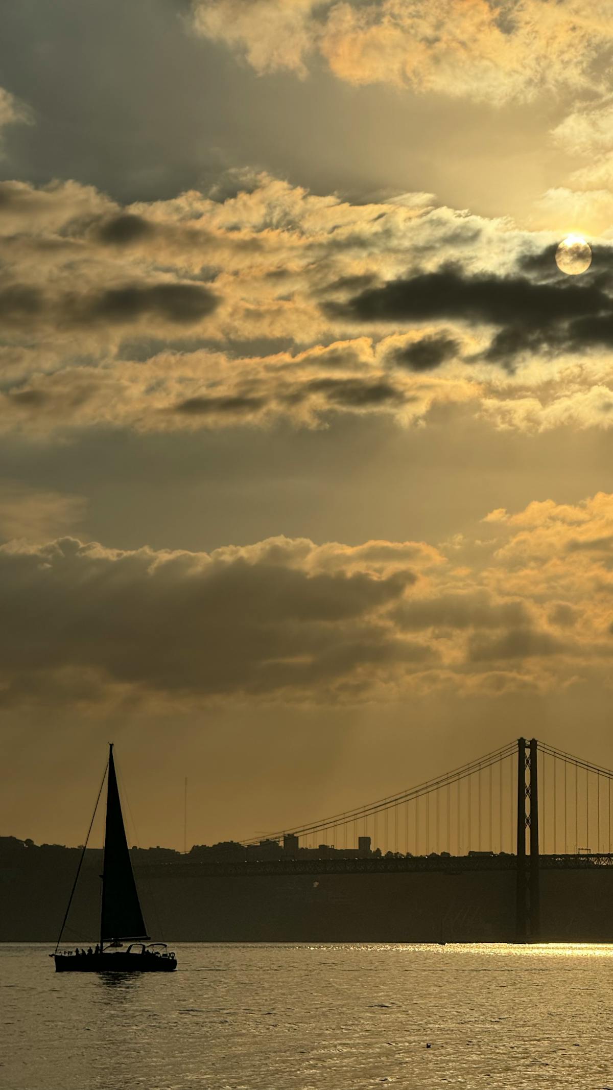 A sailboat sailing at sunset near the 25 de Abril Bridge in Lisbon