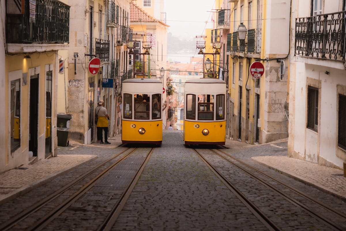 Two vintage yellow trams navigating narrow cobblestone streets in Lisbon old town