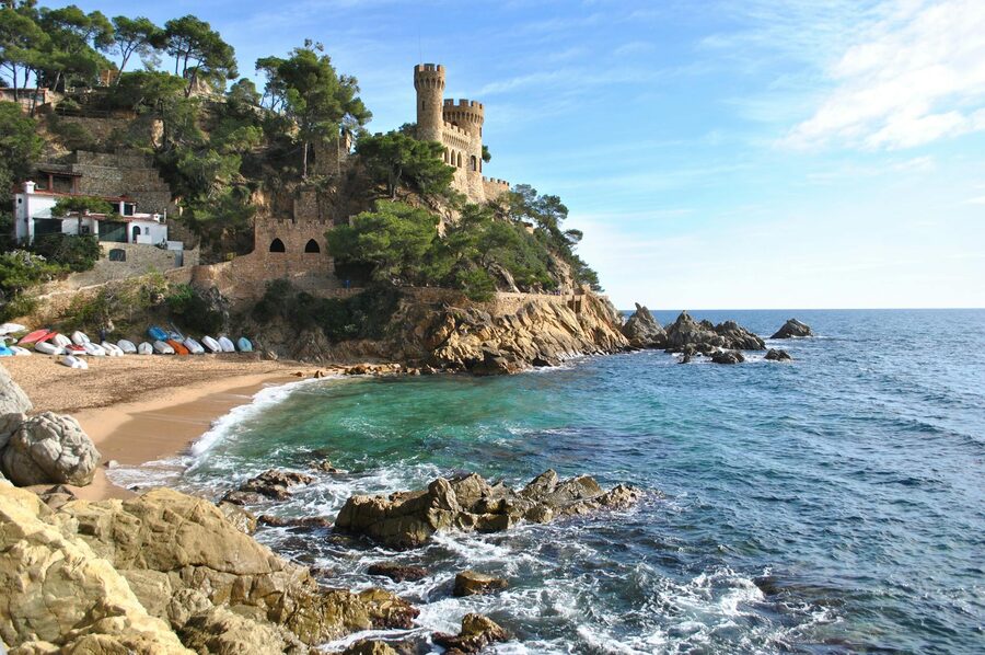 Medieval castle on rocky cliffs overlooking blue Mediterranean sea with sandy beach