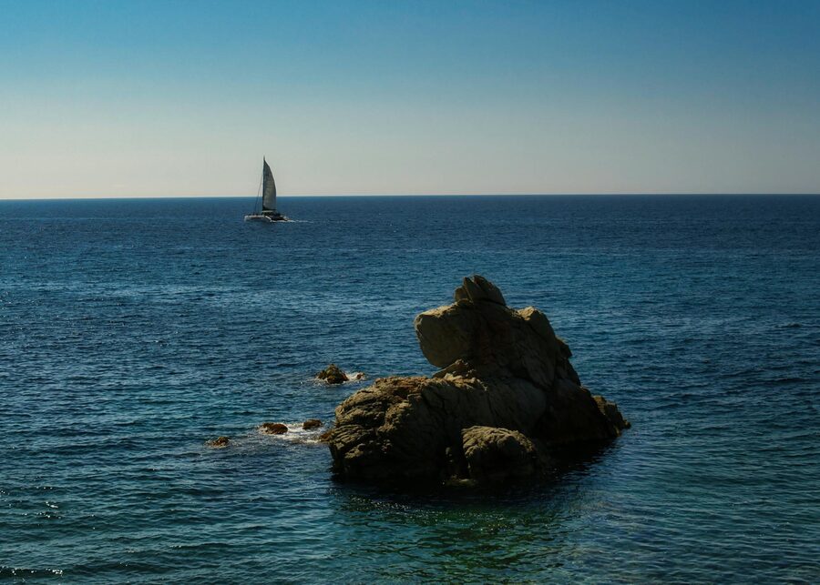 Sailboat gliding across blue waters near the rocky Costa Brava coastline