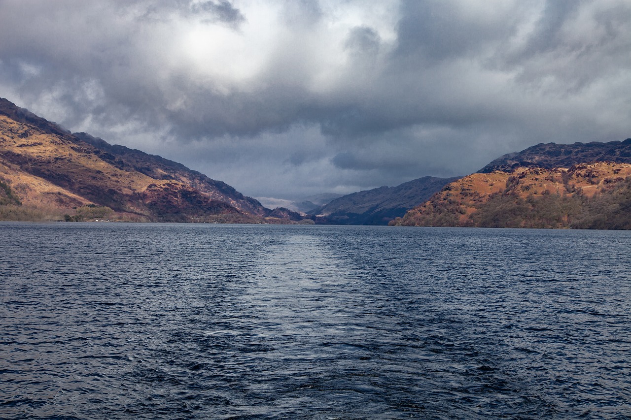Calm waters of Loch Lomond with green hills and clouds reflected in the surface