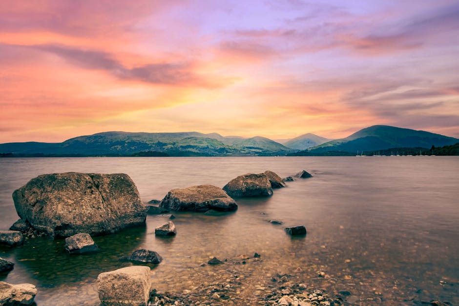Sunset light over Loch Lomond with rocks in the foreground and distant hills