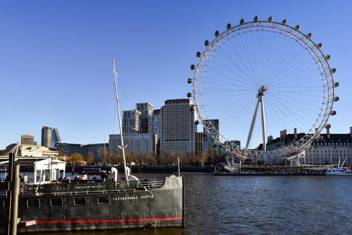 The London Eye seen from the riverside walkway with boats passing on the Thames