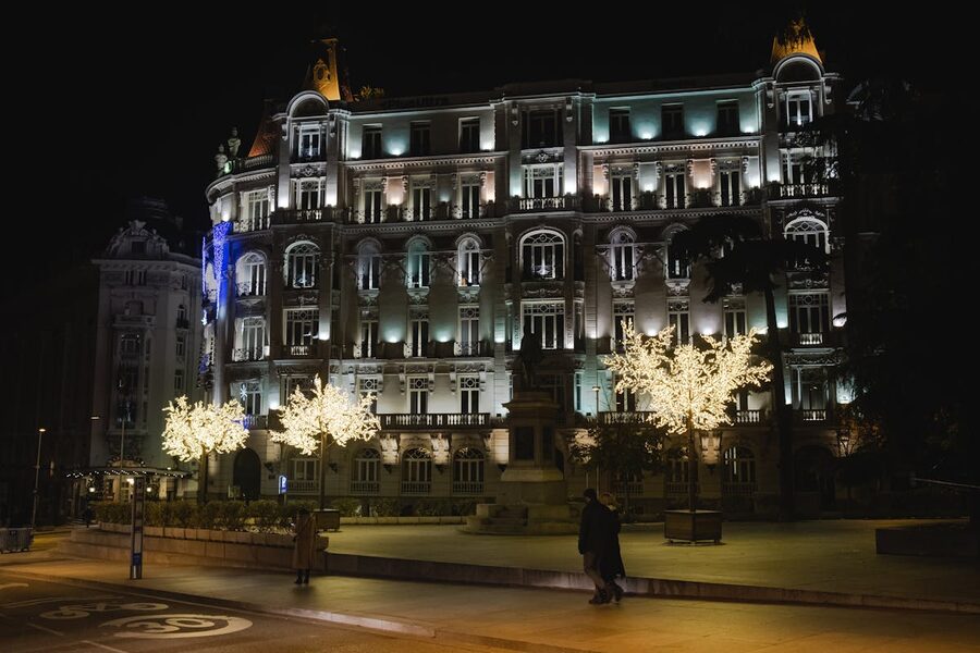 A couple walking beneath illuminated trees on a Madrid street at night