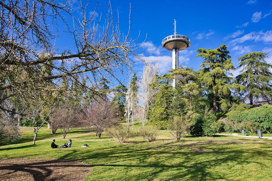 People enjoying a sunny day in a Madrid park with an observation tower
