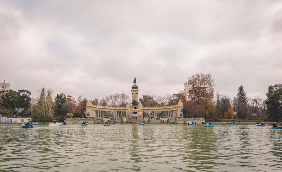 Monument and lake at El Retiro Park Madrid with boats and autumn trees