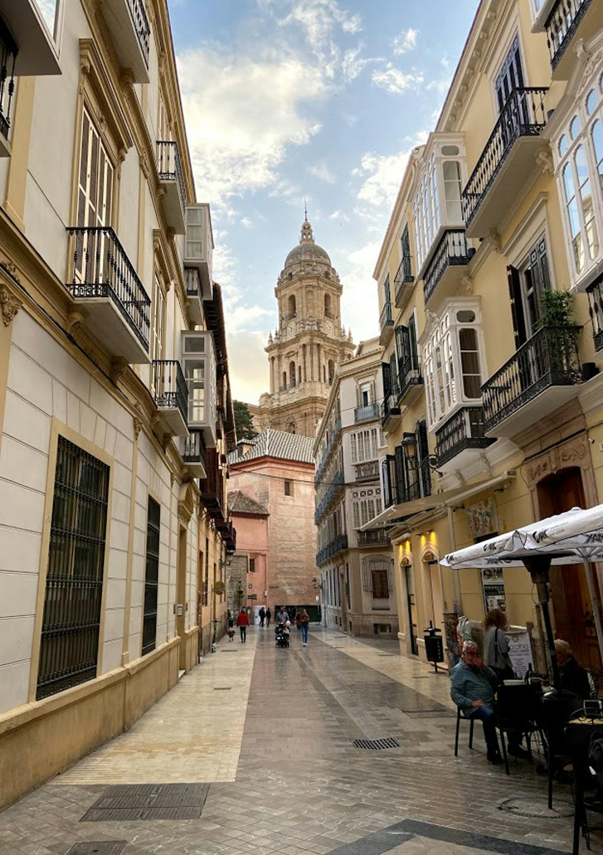 Scenic narrow alleyway in Malaga old town with the cathedral visible in the background under blue sky