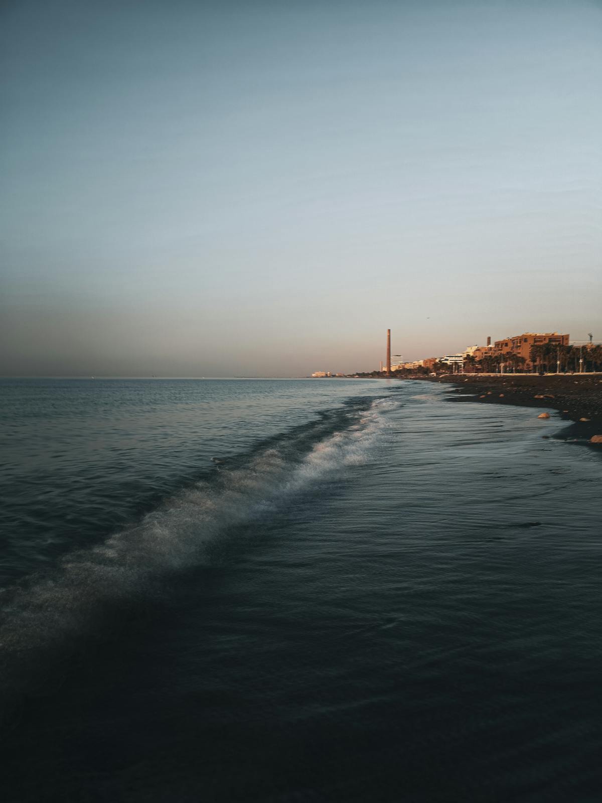 Malaga seaside beach at twilight with gentle waves and distant buildings