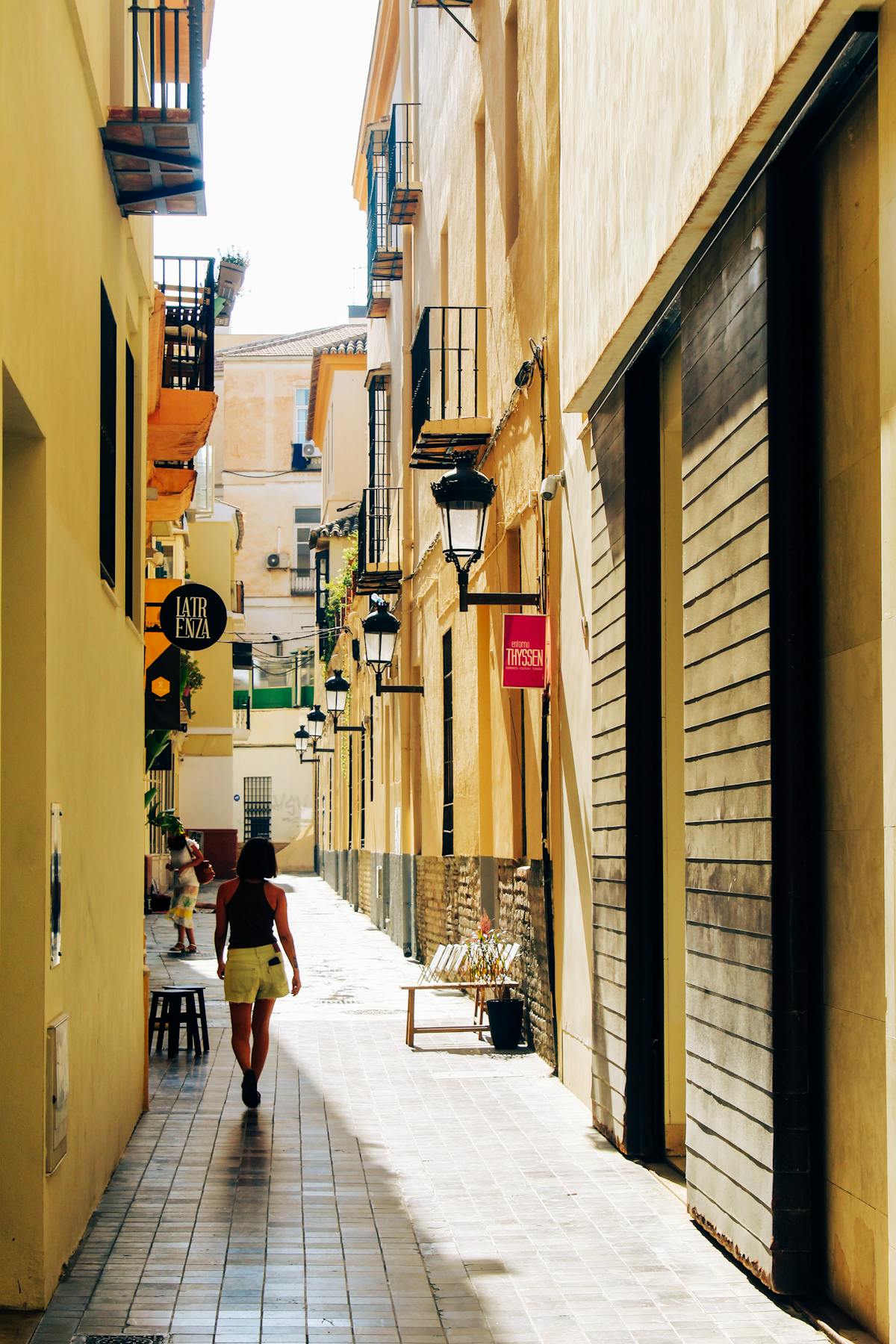A person walking through a sunlit alleyway in Malaga Spain showcasing charming historic architecture