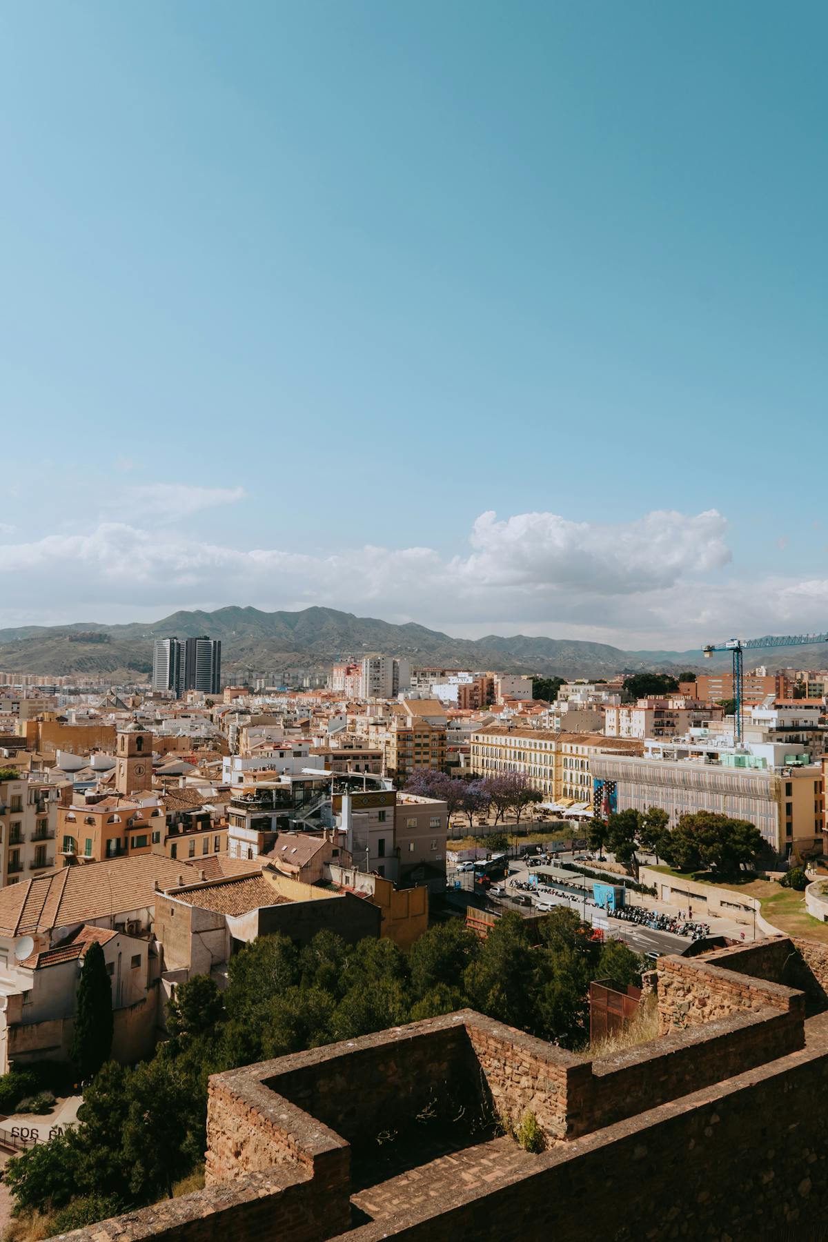 The Malaga cityscape spreading toward the mountains with Spanish architecture and vibrant urban life visible from above