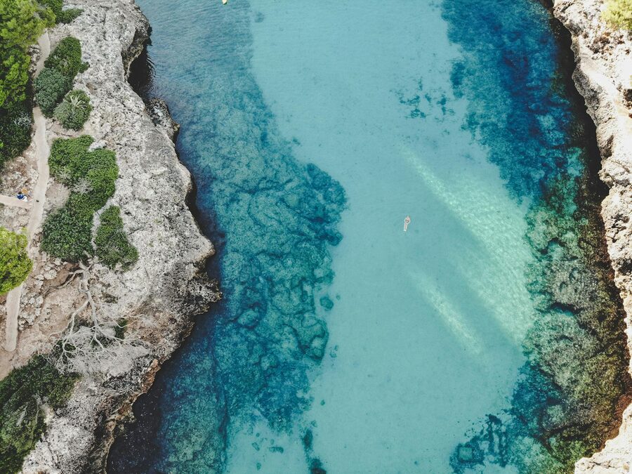 Drone view of a tranquil cove with clear blue sea and rocky cliffs