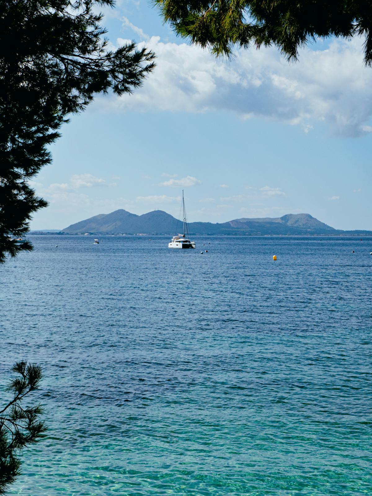 Sailboat on the open sea with the island of Mallorca visible in the background under a bright summer sky