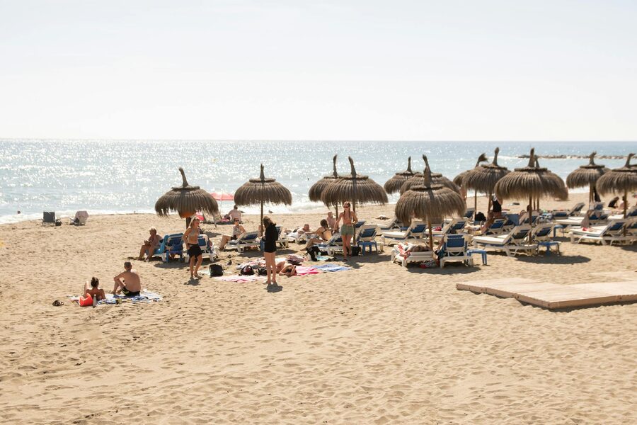 Sunny day on Marbella beach with straw umbrellas and clear sea view