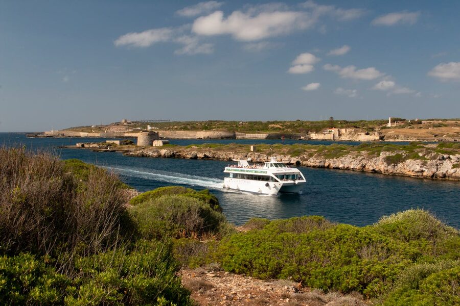Boat tour passing a historic defense tower on the coast of Menorca