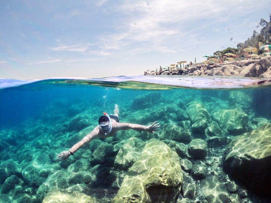 Person snorkeling in clear water near a rocky Mediterranean coastline