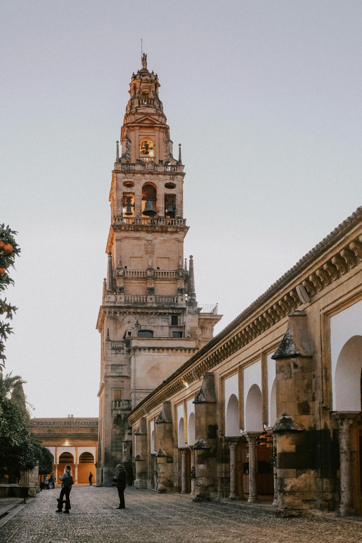 The iconic tower of the Mosque-Cathedral of Cordoba lit up at dusk against a purple sky