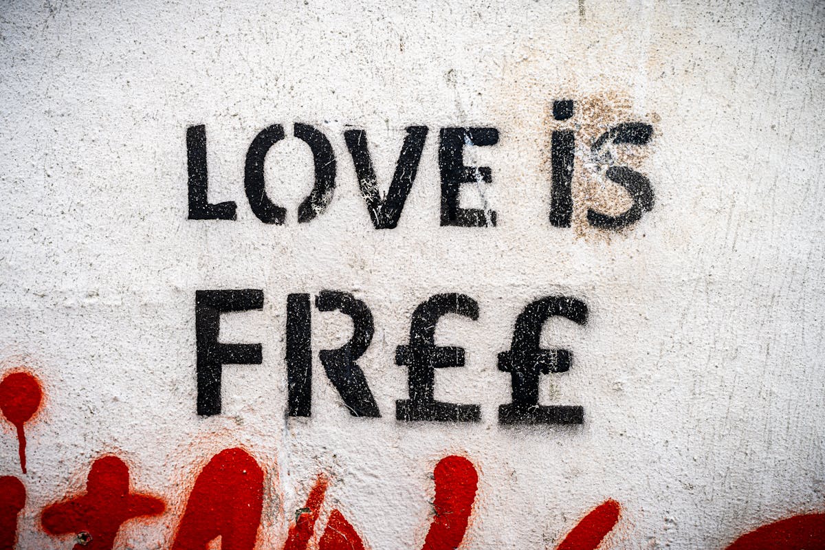 Street art stencil reading Love is Free on an urban wall