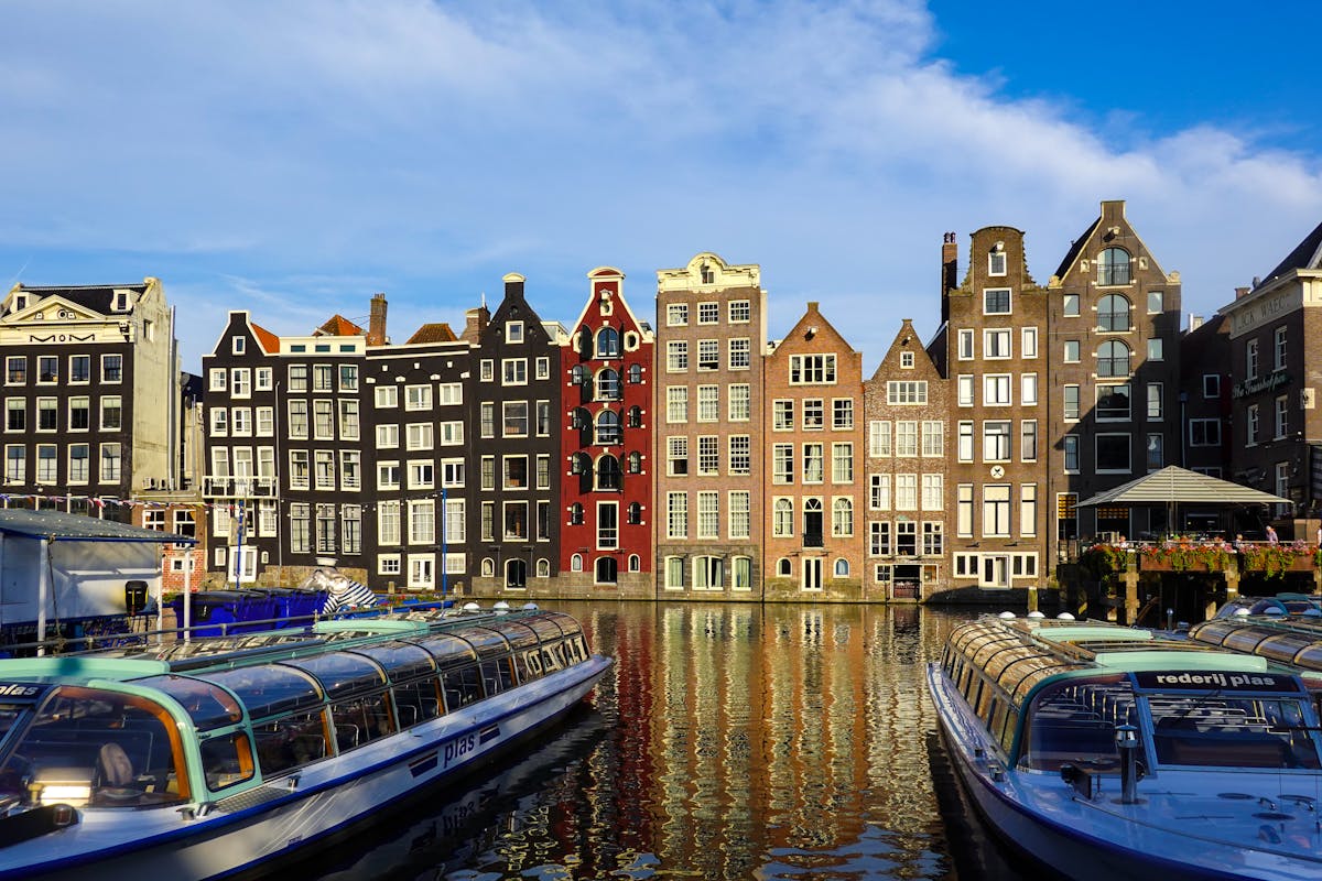 Colorful historic buildings along Amsterdam canals with boats in calm water