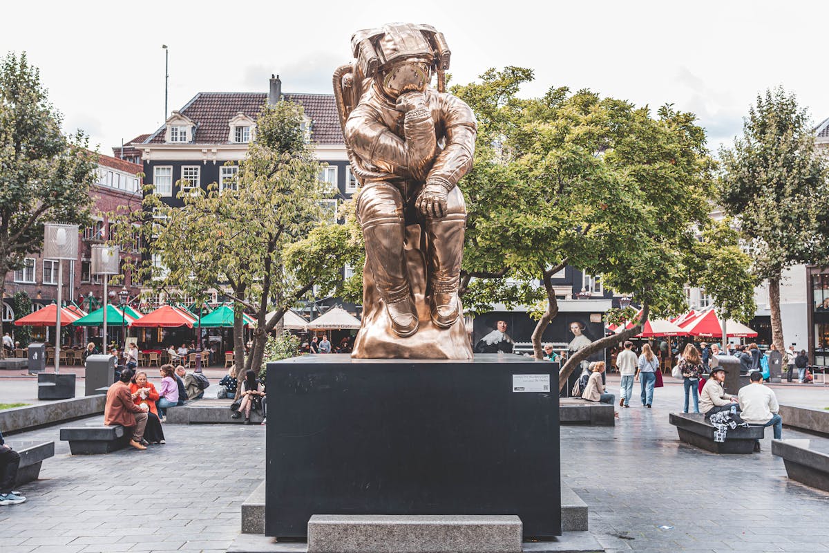 Golden astronaut sculpture in an Amsterdam square with people nearby