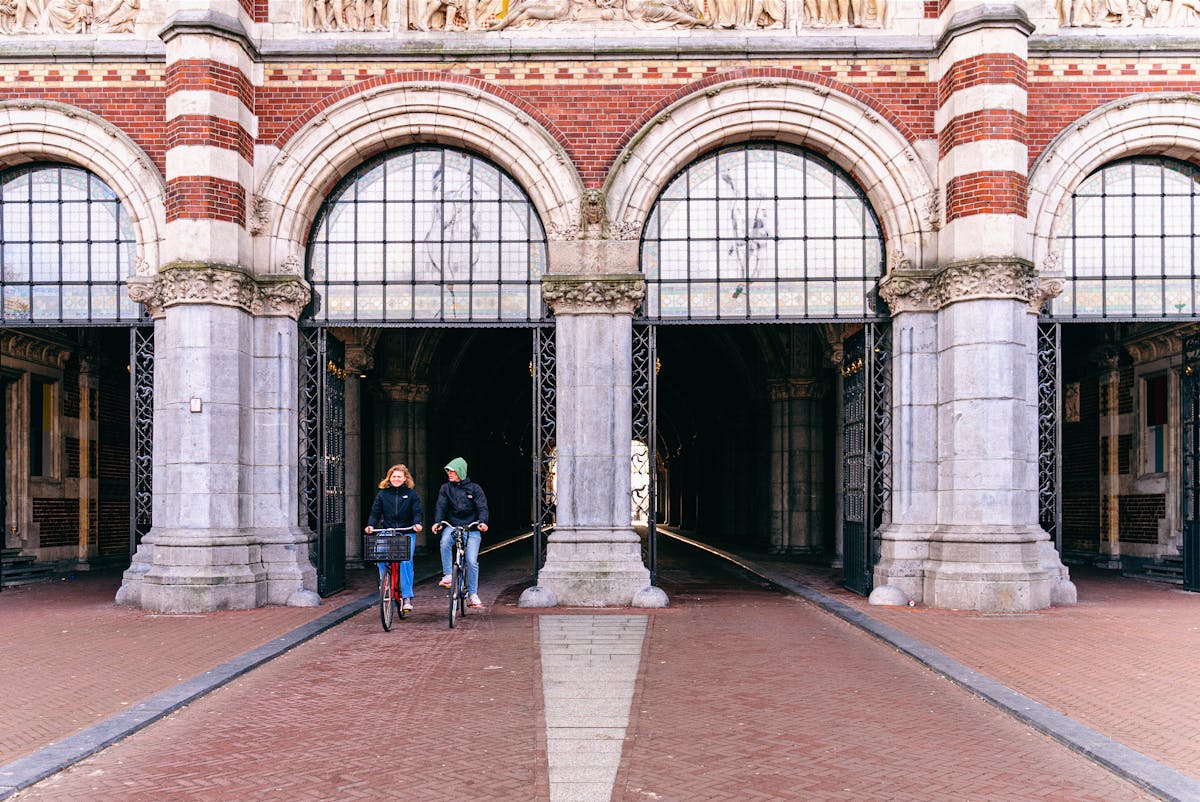 Two cyclists riding through the Rijksmuseum archway in Amsterdam