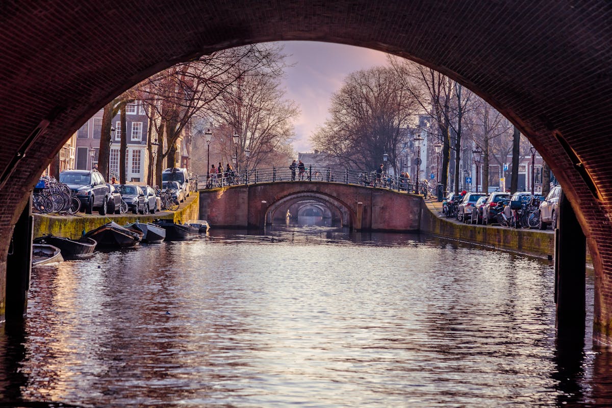 View of Amsterdam canal framed through a bridge arch showing historic architecture
