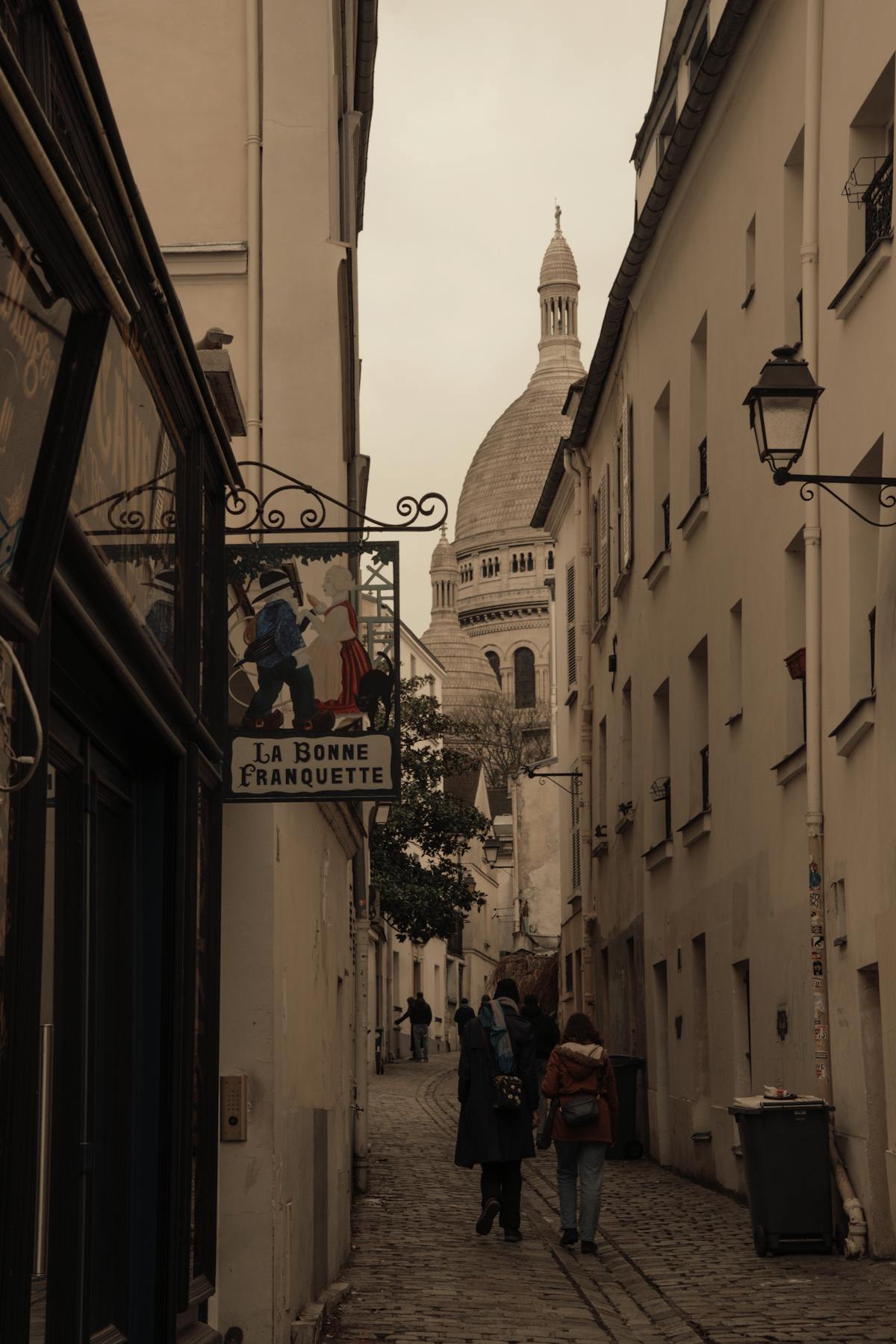 Narrow Parisian street in Montmartre with the Sacre-Coeur dome visible in the background