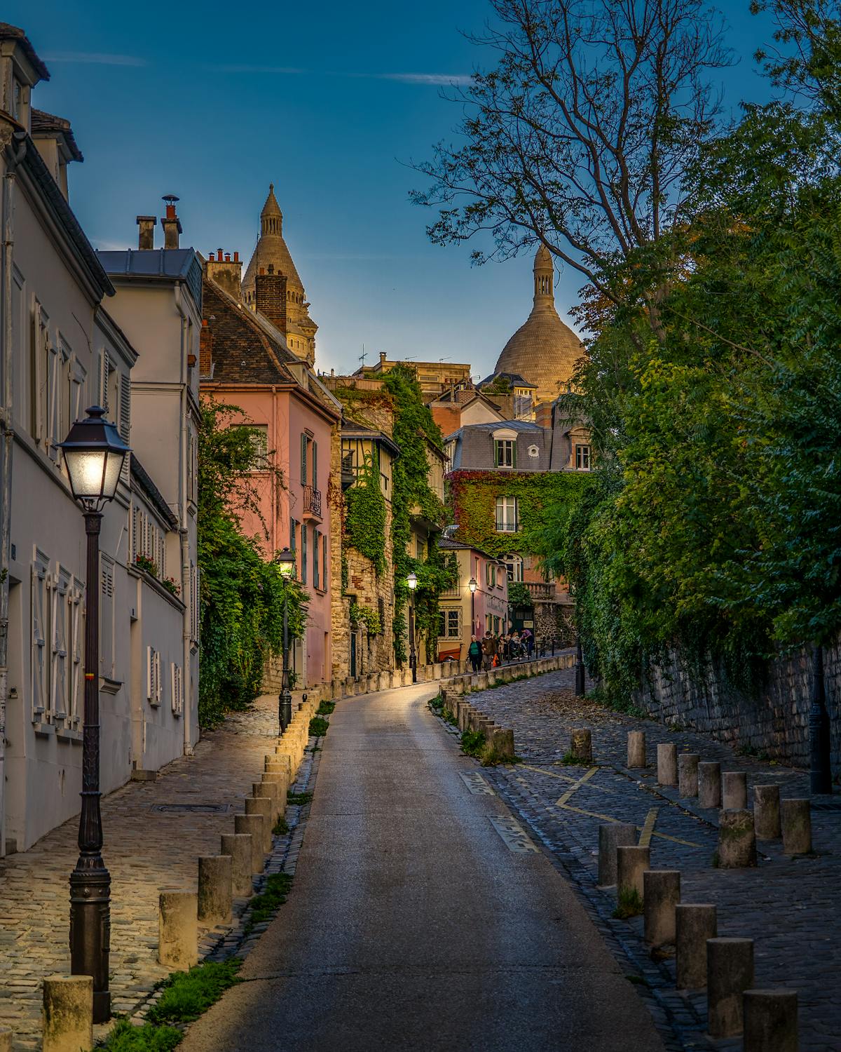 A quiet Montmartre street in Paris at dusk with warm light from cafe windows