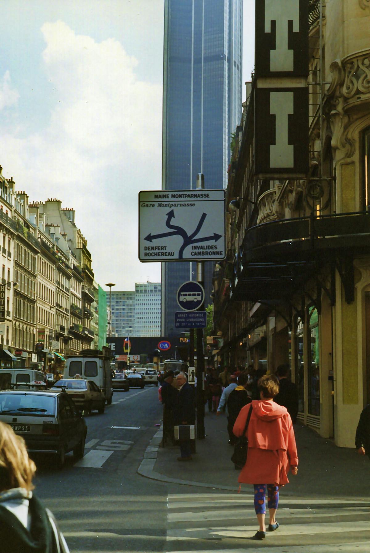 A Paris street with cafes and pedestrians with the Montparnasse Tower visible in the background