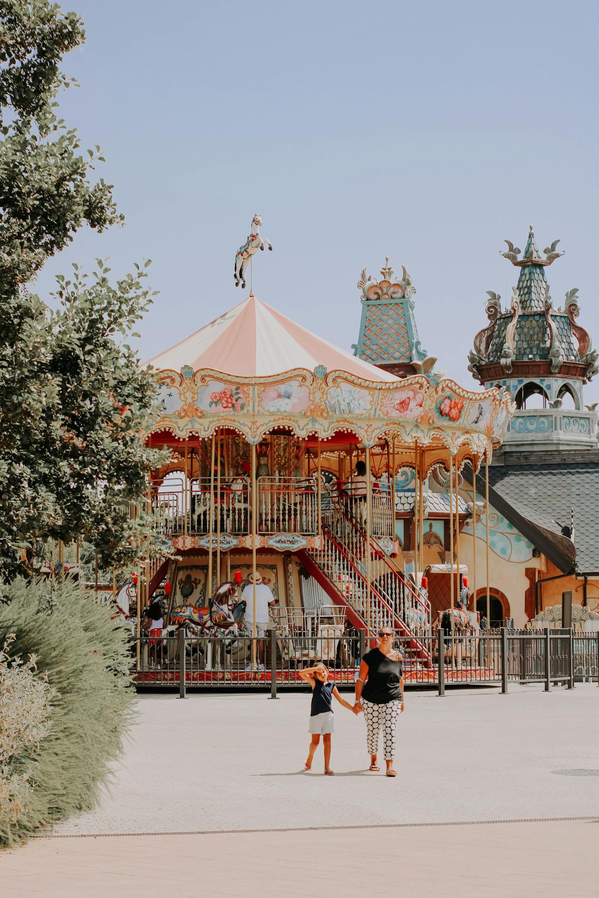 Mother and daughter walking near a colorful carousel at an amusement park