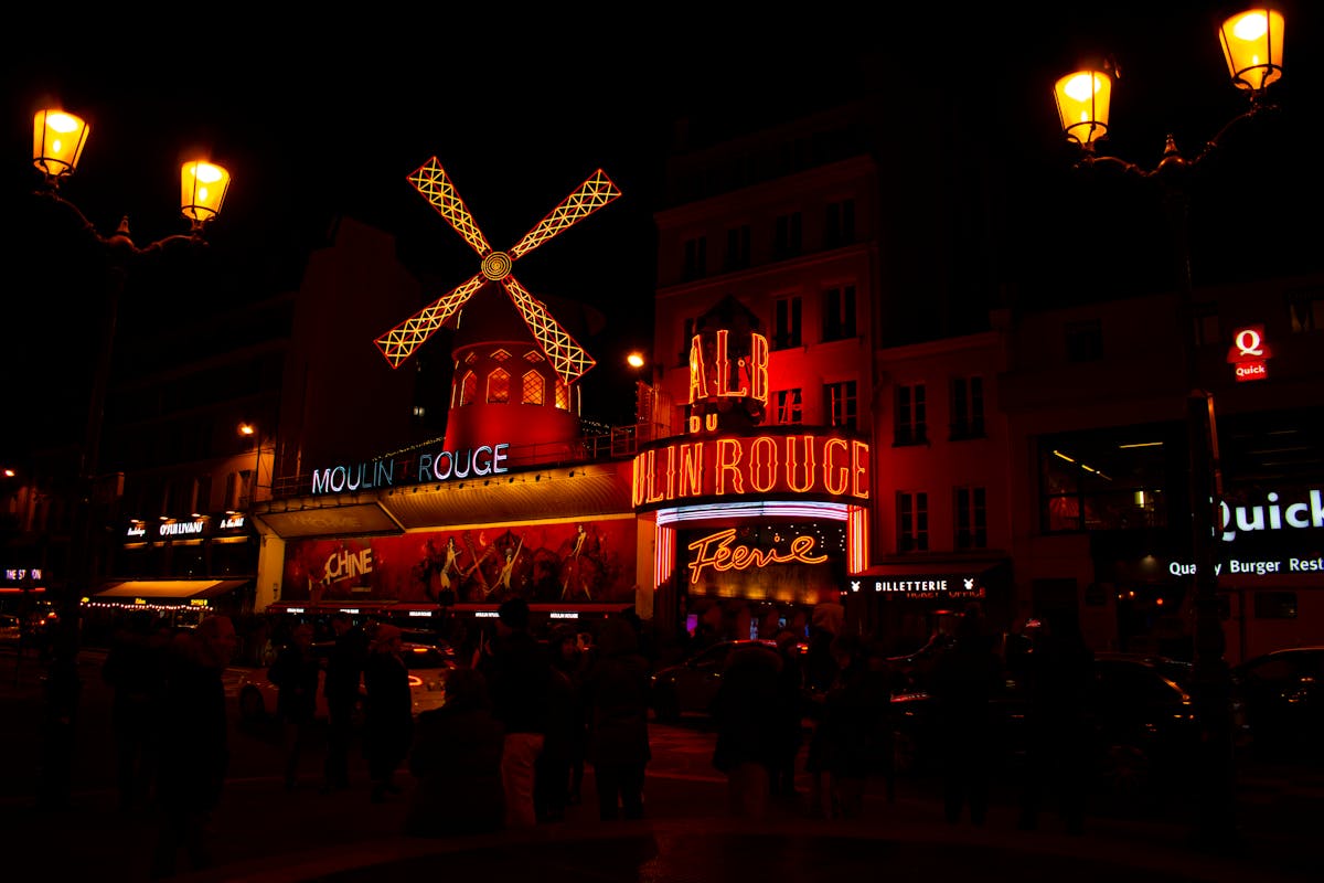 The Moulin Rouge illuminated at night with its red windmill lit up and crowds gathered below