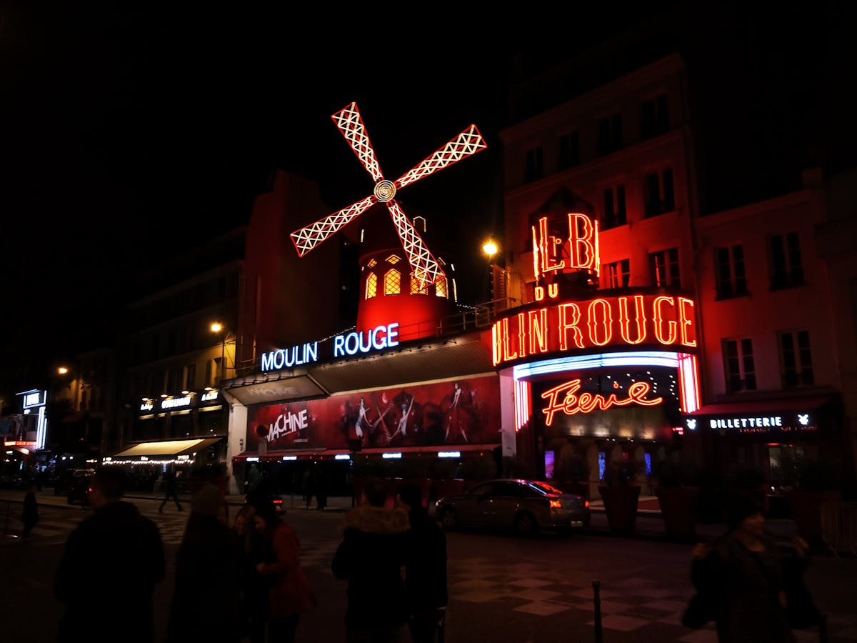 The Moulin Rouge exterior at night with neon signs glowing and the red windmill spinning above
