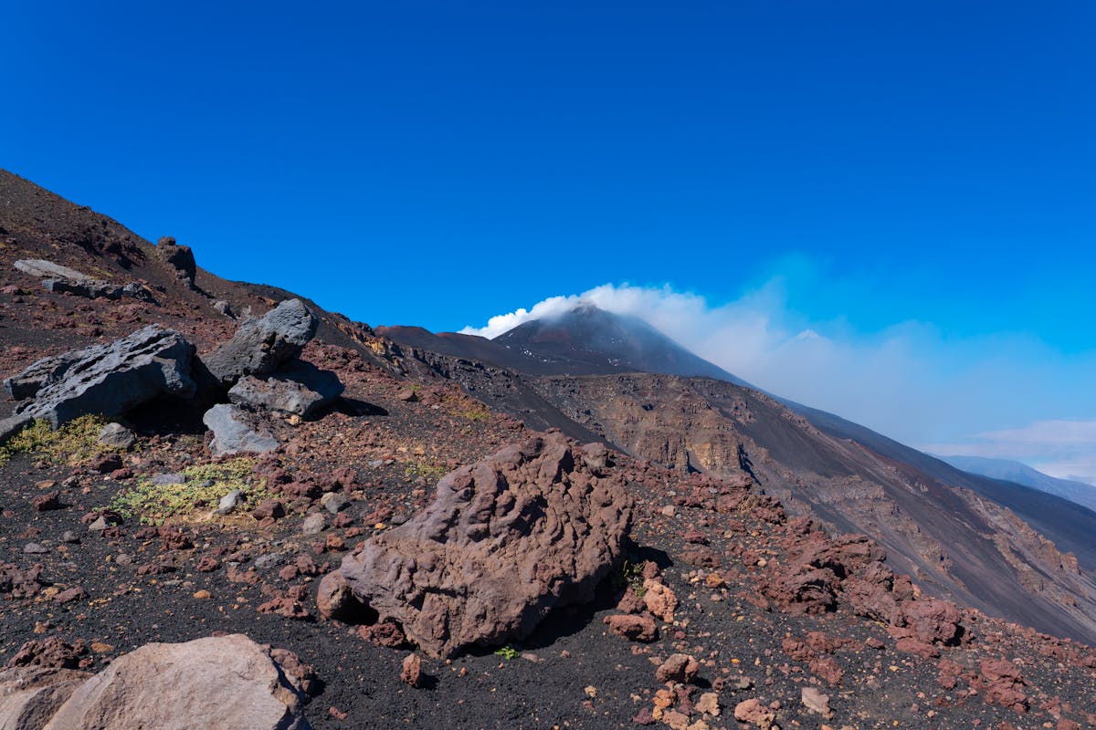 Sea of clouds below the summit of Mount Etna with volcanic terrain in foreground