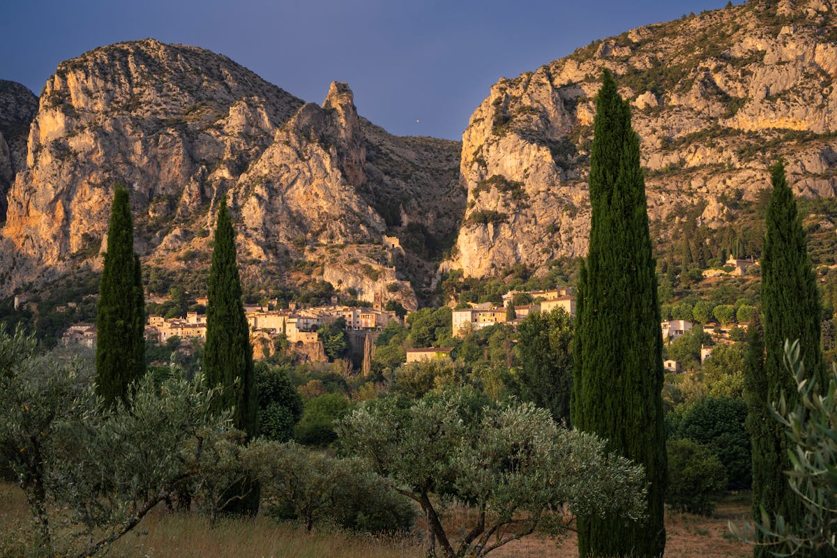 Moustiers-Sainte-Marie village with cypress trees and cliffs during golden hour in Provence France