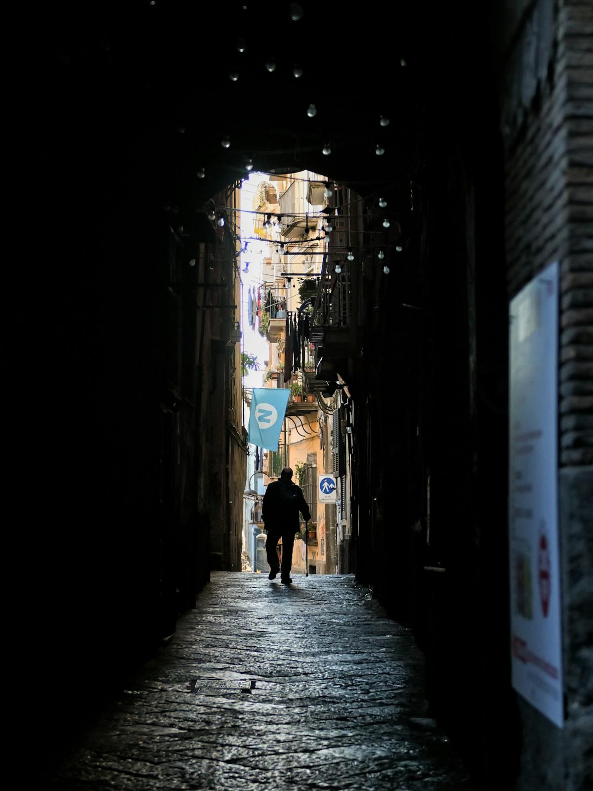 A mysterious figure walks through a narrow alley in Naples