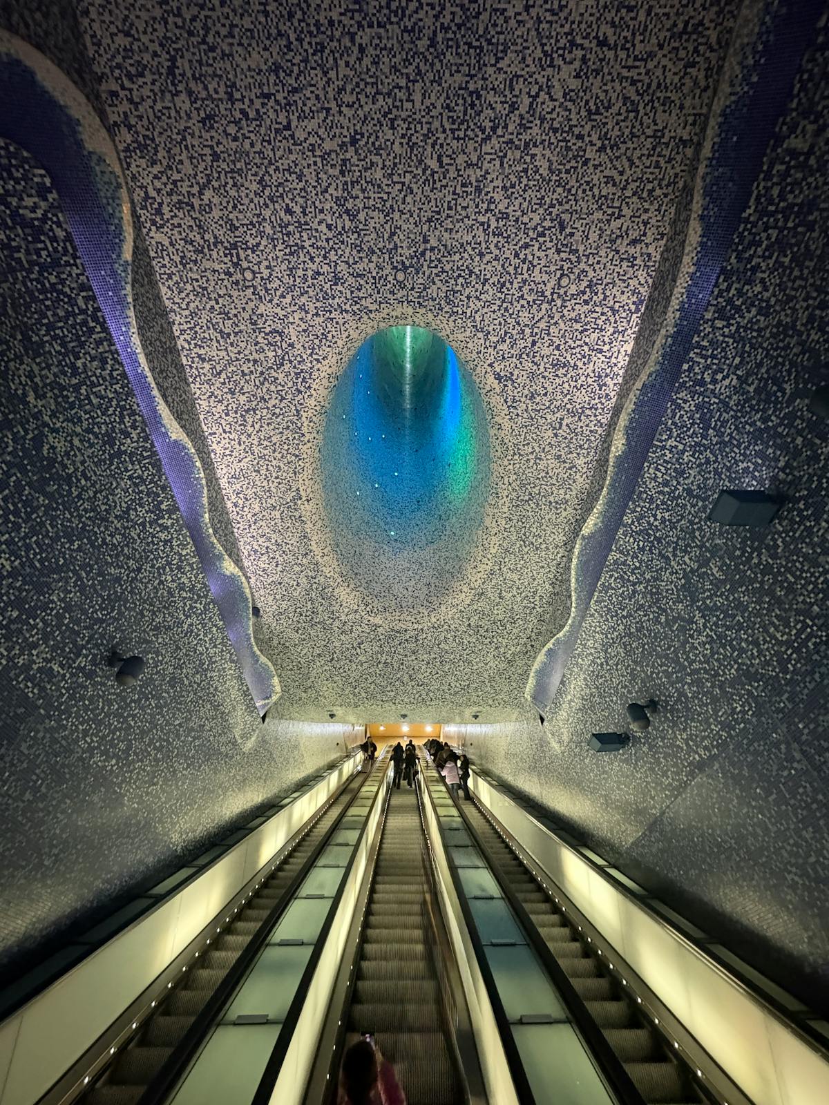 Artistic colorful ceiling design of metro station in Naples Italy with people on escalator