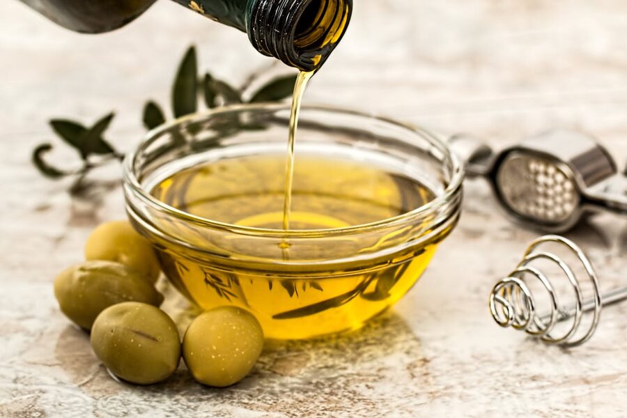 Close-up of olive oil being poured into a glass bowl with fresh olives