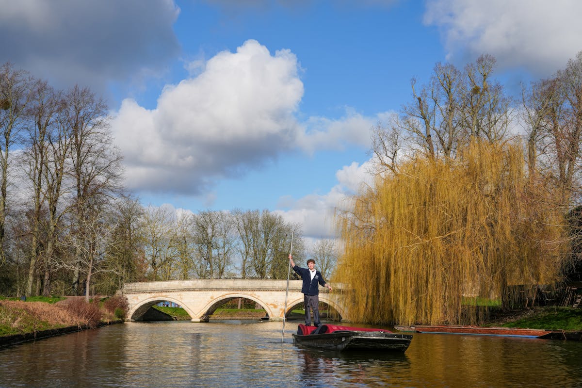 Person punting a boat under a stone bridge in Oxford on a sunny day