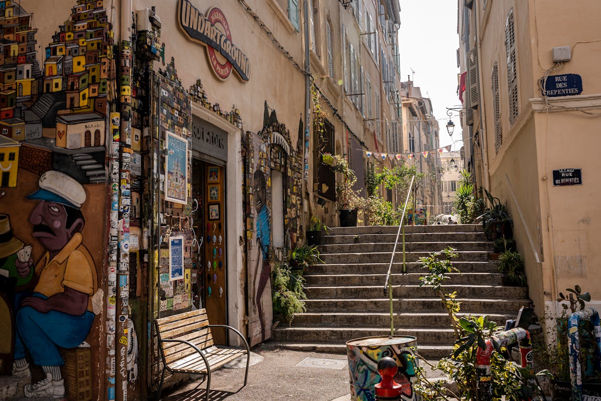 Sunlit narrow street in Marseille's Le Panier district with murals and plants