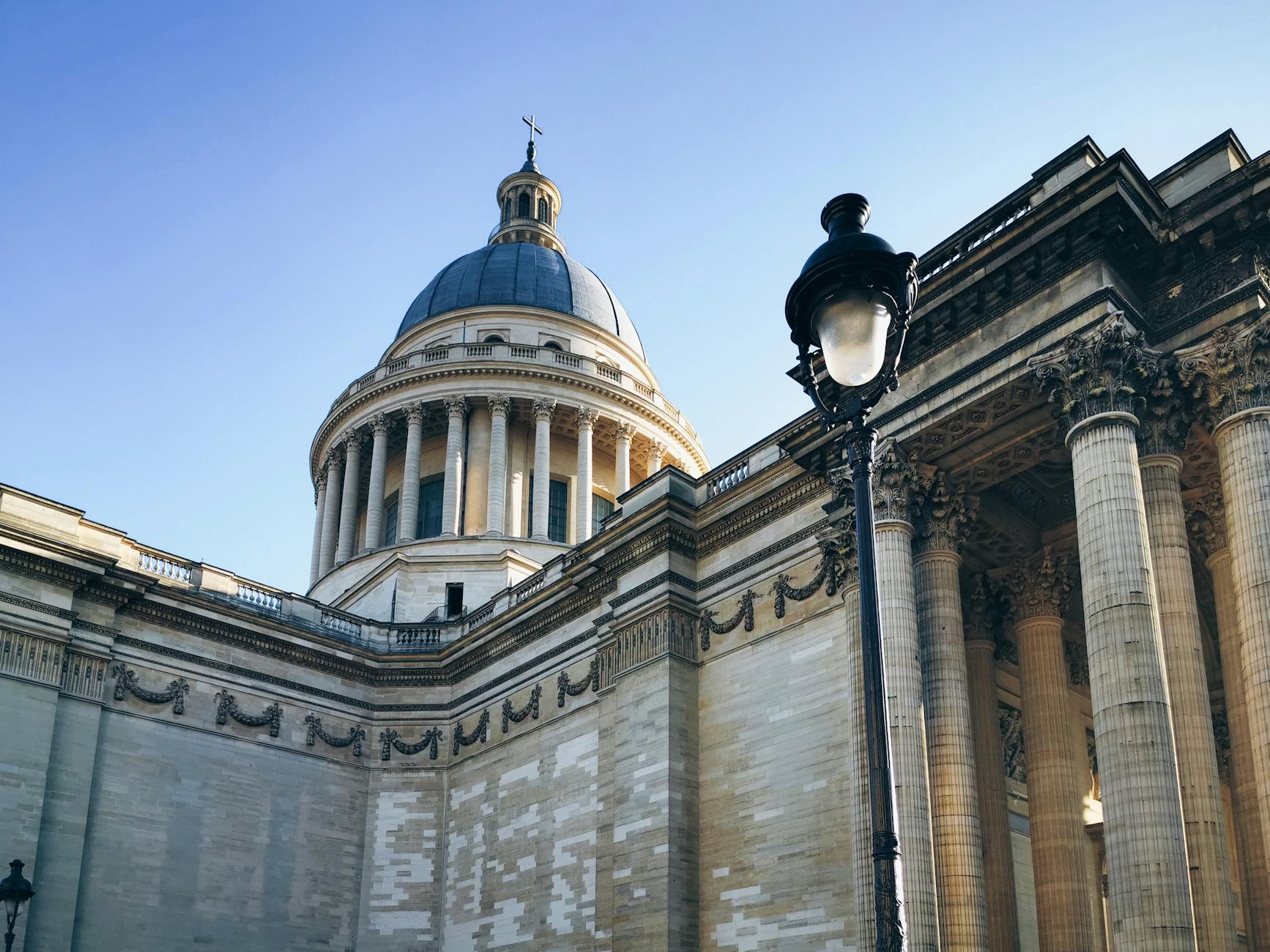 The neoclassical facade of the Pantheon in Paris with tall Corinthian columns under a clear sky