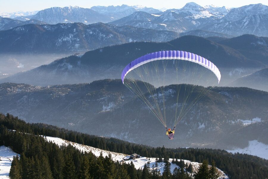 Paraglider flying above fog-covered Alpine mountains in winter