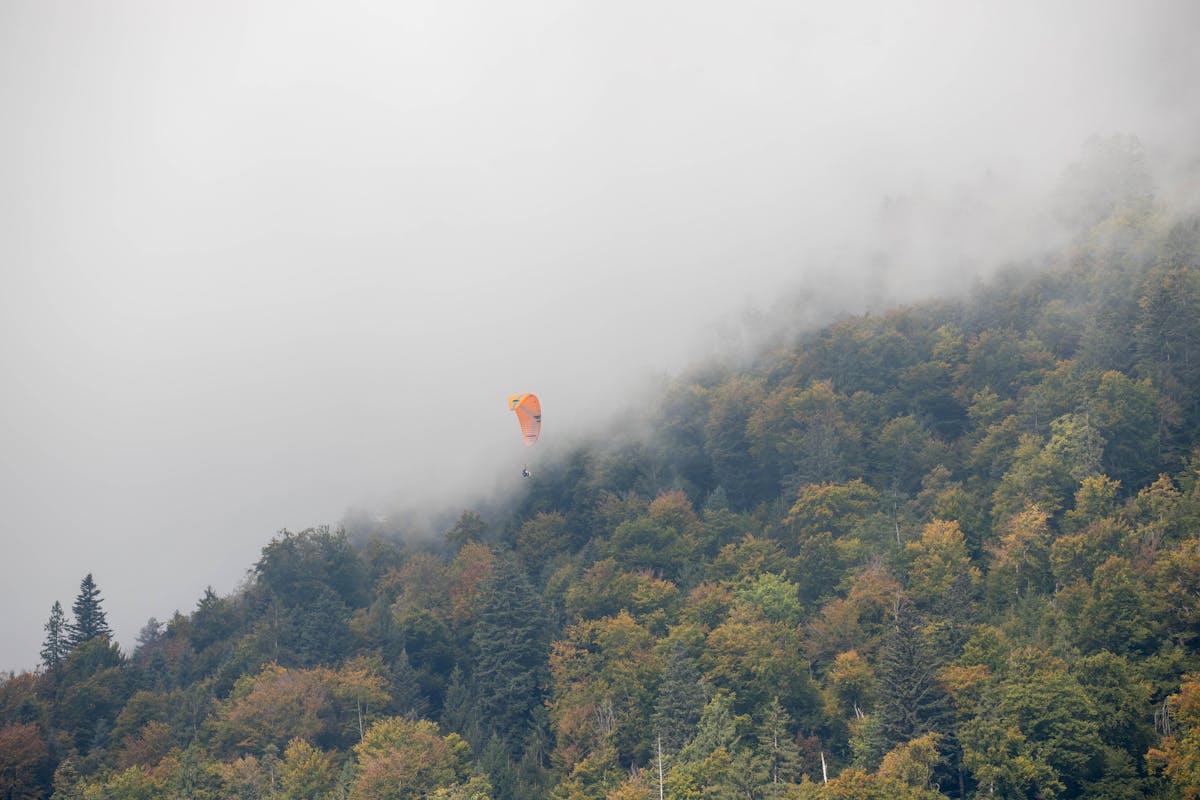 Paraglider flying above foggy Swiss forest near Interlaken Switzerland